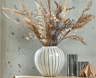 Graue Vase mit vertikalen Streifen und Kunstblumen auf einer Anrichte