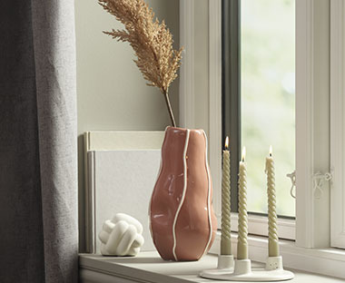 Vase in Rosa aus Dolomit auf einem Fensterbrett neben Kerzen