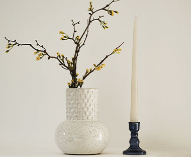 Weiße Vase mit Dekozweigen neben einem Kerzenständer auf einem Tisch