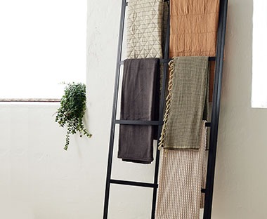 Kuscheldecken in verschiedenen Designs auf einem Leiterregal hängend