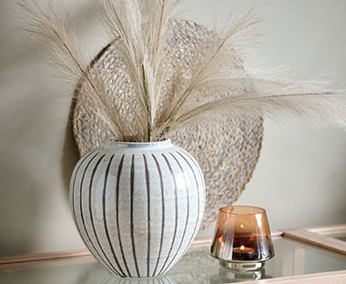Rundes Tischset auf einer Kommode an einer Wand lehnend hinter einer Vase