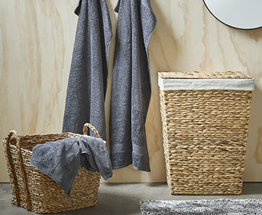Ein Wäschekorb in Natur neben einem Korb und Handtücher